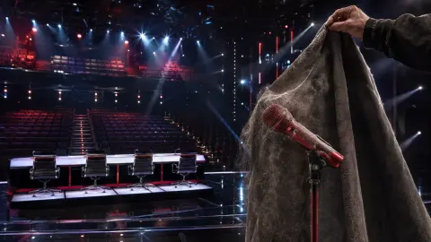 Television talent-show judges' desk under spotlights in an otherwise empty studio.