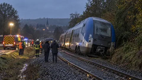 Editorial illustration of a French regional train derailed beside a wooded embankment as emergency crews respond