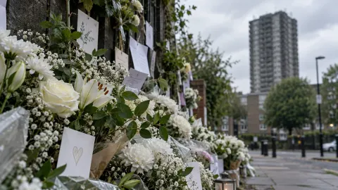 Editorial illustration of white flowers at a London memorial wall with a blurred tower beyond