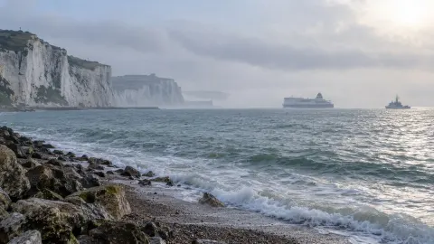 Editorial illustration of the English Channel coast with distant ferry and patrol vessel