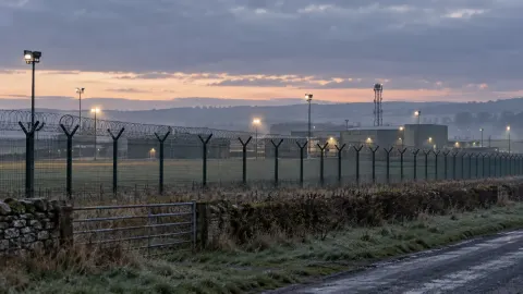 Editorial illustration of a generic British military base perimeter at dawn